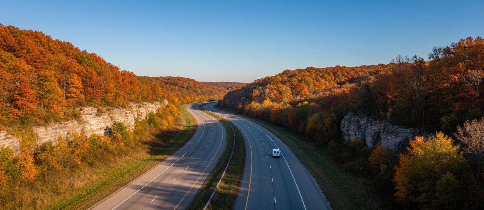 An empty interstate curving through autumn hills and limestone cuts in Kentucky, one white van far ahead